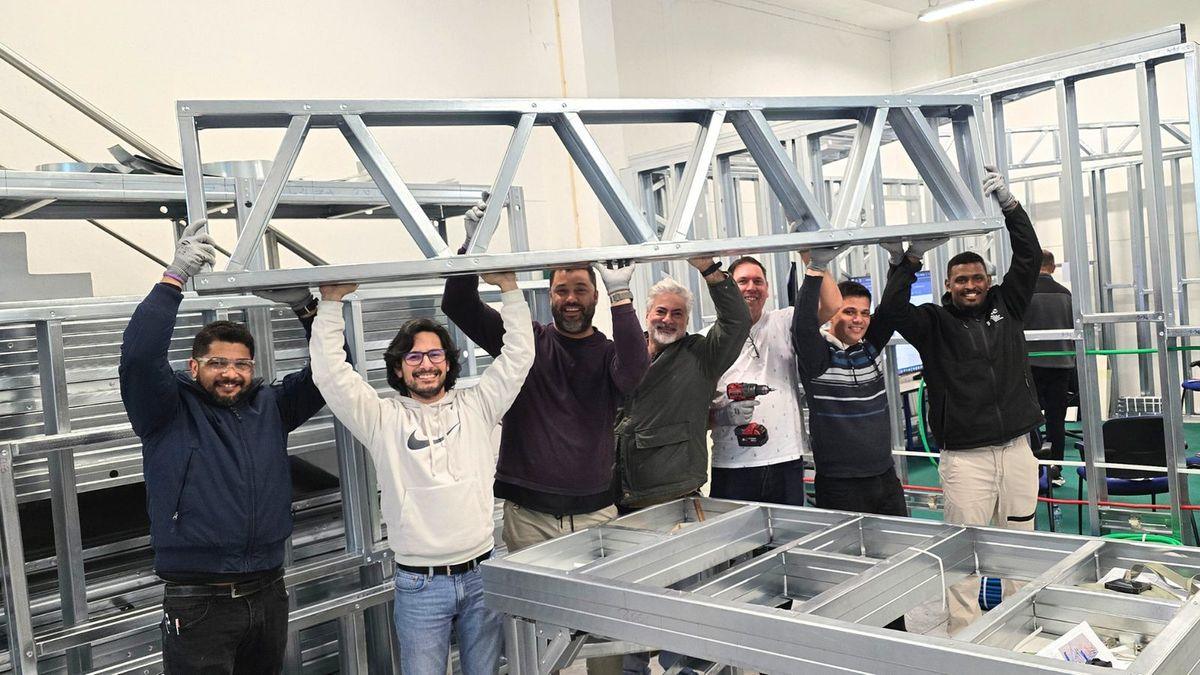 Grupo de formandos a levantar em conjunto uma treliça em perfis de light steel
              frame, dentro das instalações da ConstruÁgil.