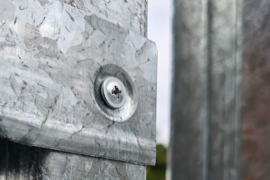 Pormenor macro de dois perfis em aço galvanizado unidos por parafuso
              autoperfurante, com a textura da galvanização à vista.